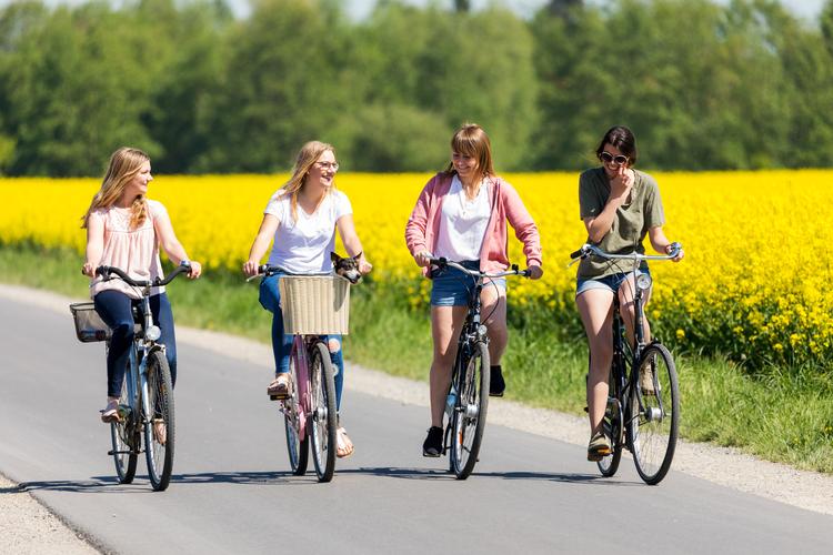 Vier Frauen fahren Fahrrad auf einer Landstraße neben einem Rapsfeld in Olpenitz